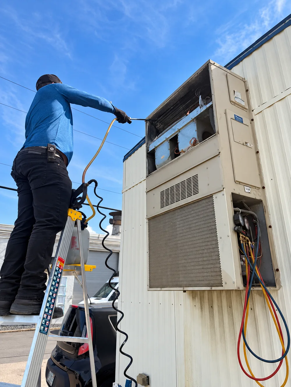 Technician servicing the exposed coil of a wall-mounted outdoor AC unit